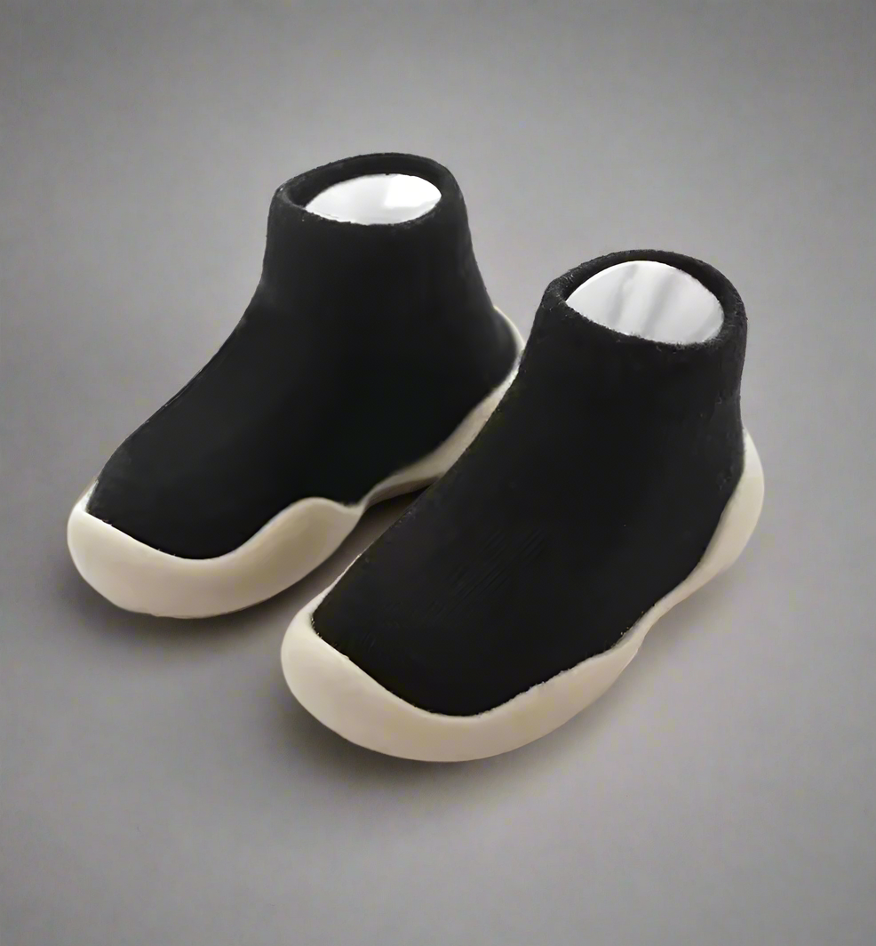 Pair of black slip-on shoes with white soles on a gray background