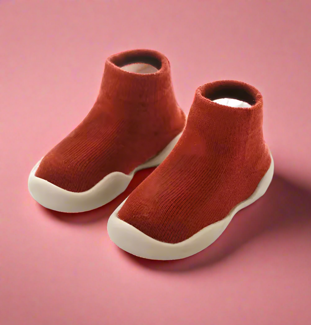 Red children's shoes with white soles on a pink background