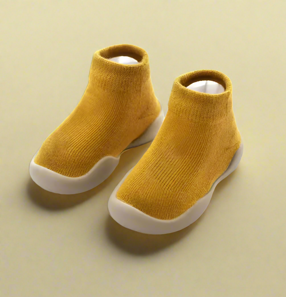 Pair of mustard yellow ankle boots with white soles on a beige background